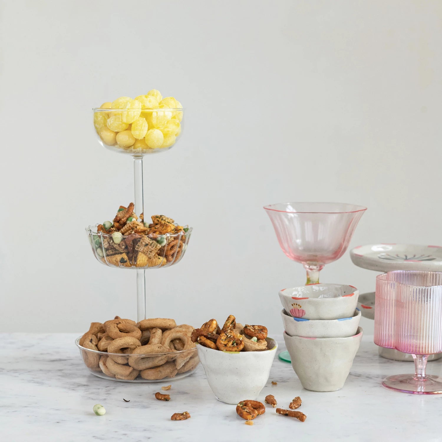 three-tiered glass tray serving candy and nuts on neutral background