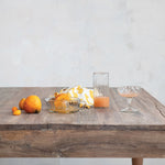 clear glass pressed juicer with handle and pour spout, displayed on rustic wooden table with fresh fruit