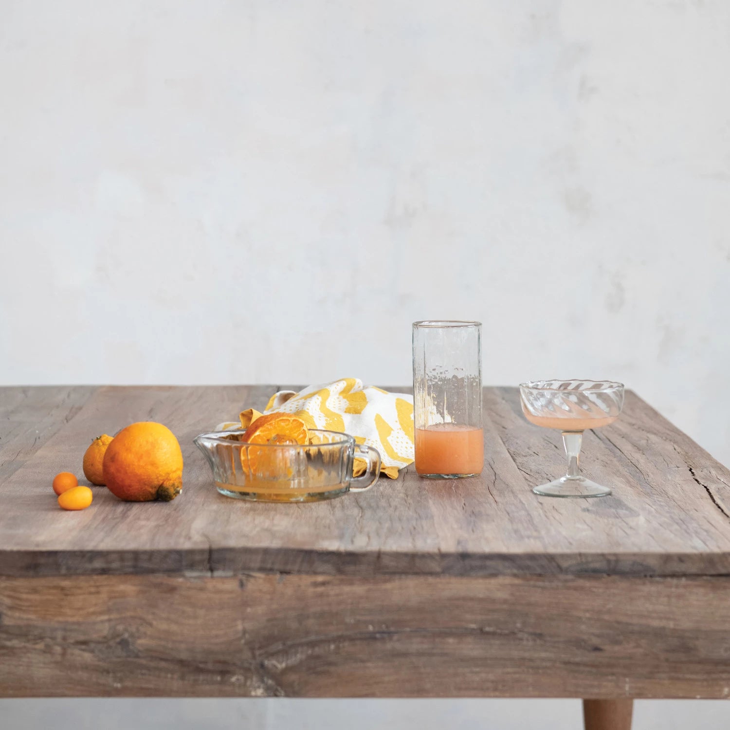 clear glass pressed juicer with handle and pour spout, displayed on rustic wooden table with fresh fruit