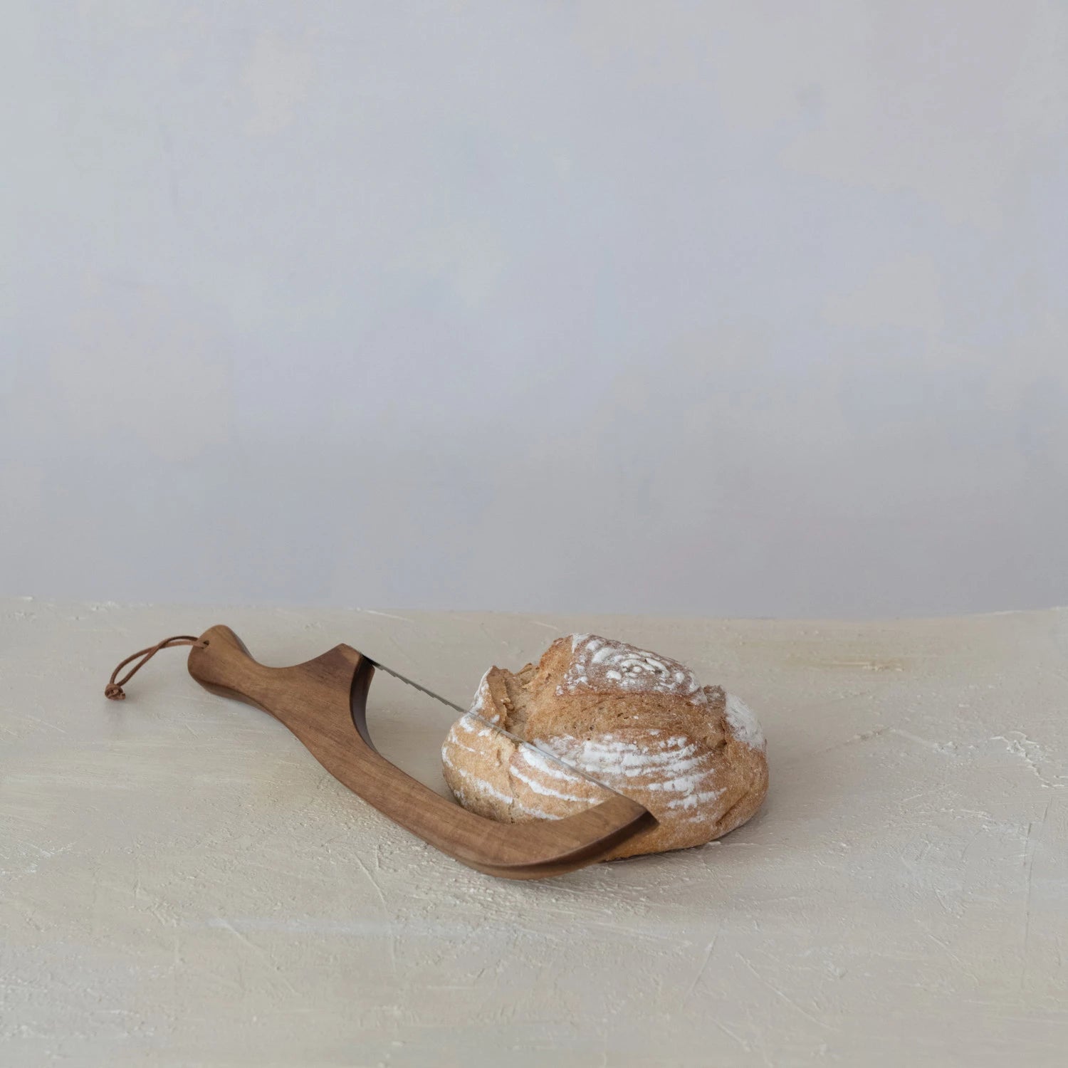 Wooden bread knife with a loaf of bread on a light surface