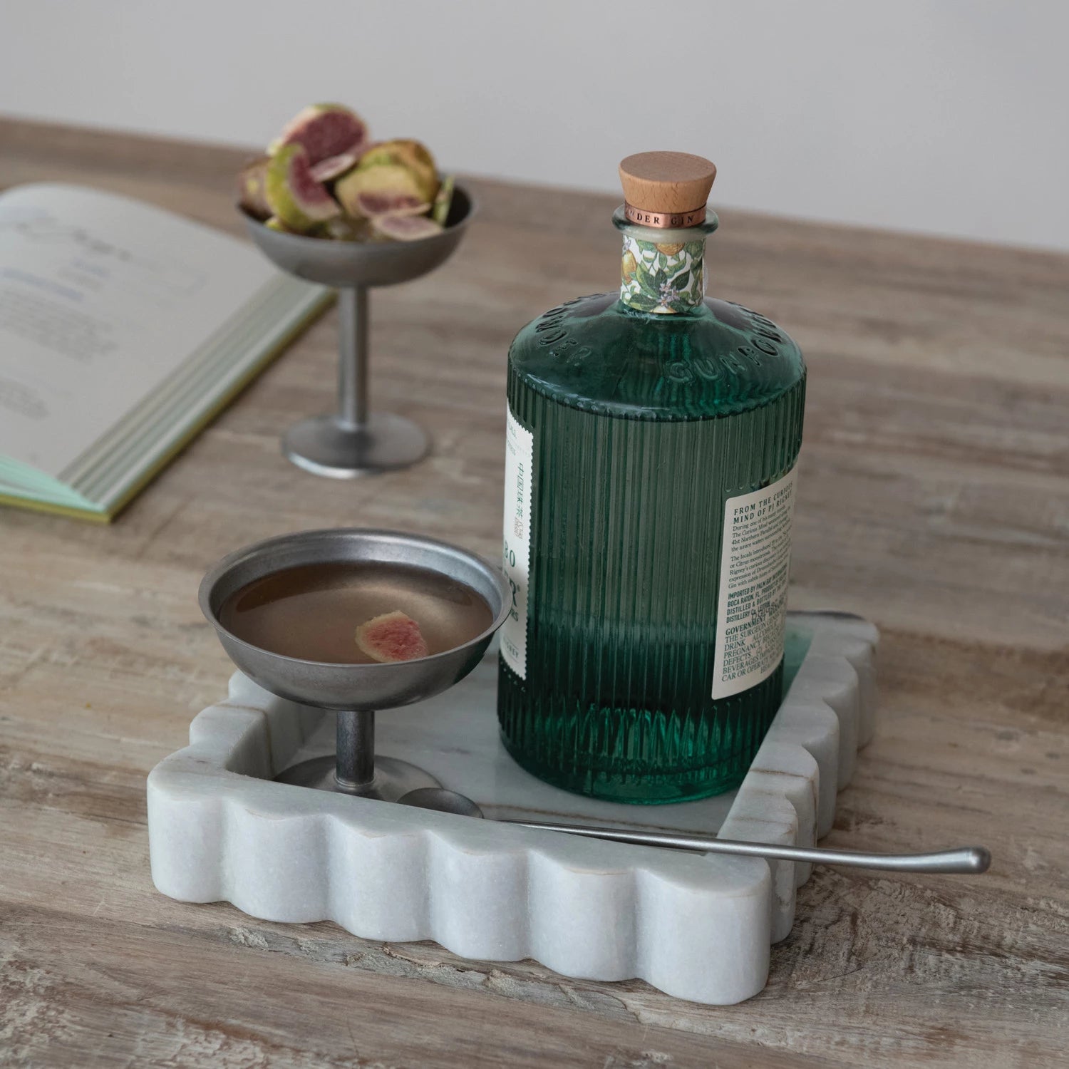 square grey marble tray with scalloped edge, styled with green glass bottle and metal cocktail dish on a wooden surface