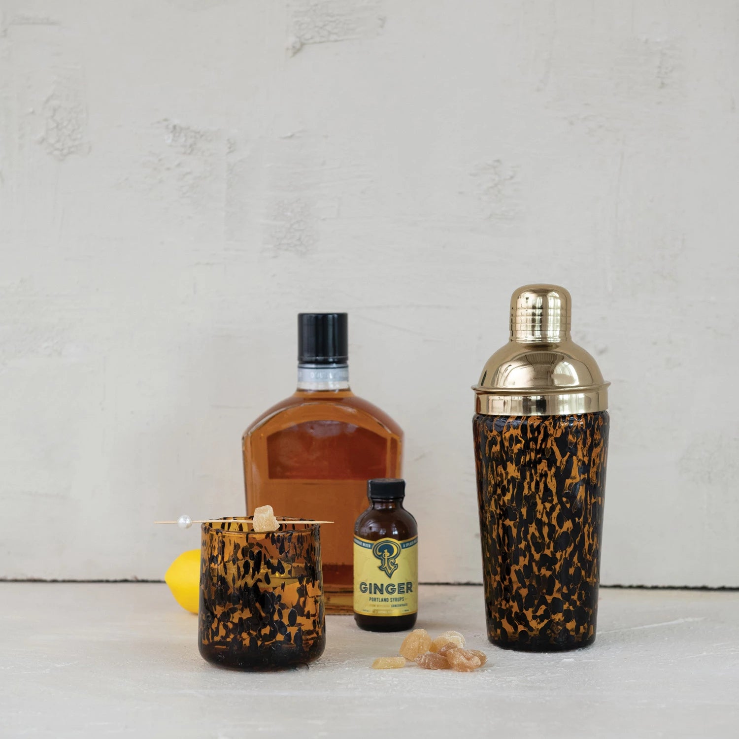 Bottle of Johnnie Walker whiskey, a small bottle of ginger liqueur, a cocktail shaker with a leopard print design, and a tortoiseshell drinking glass