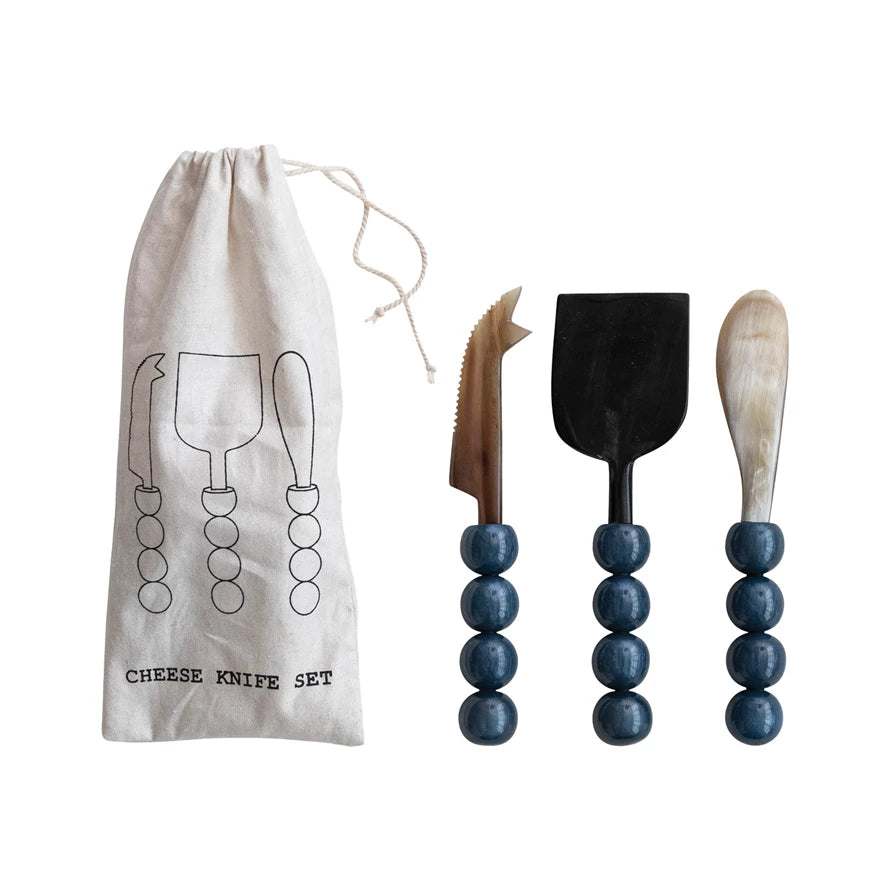 Set of cheese knives with blue bead handles and a branded drawstring bag on a white background
