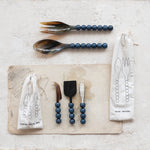 Set of salad servers with blue beaded handles on a light surface with packaging.