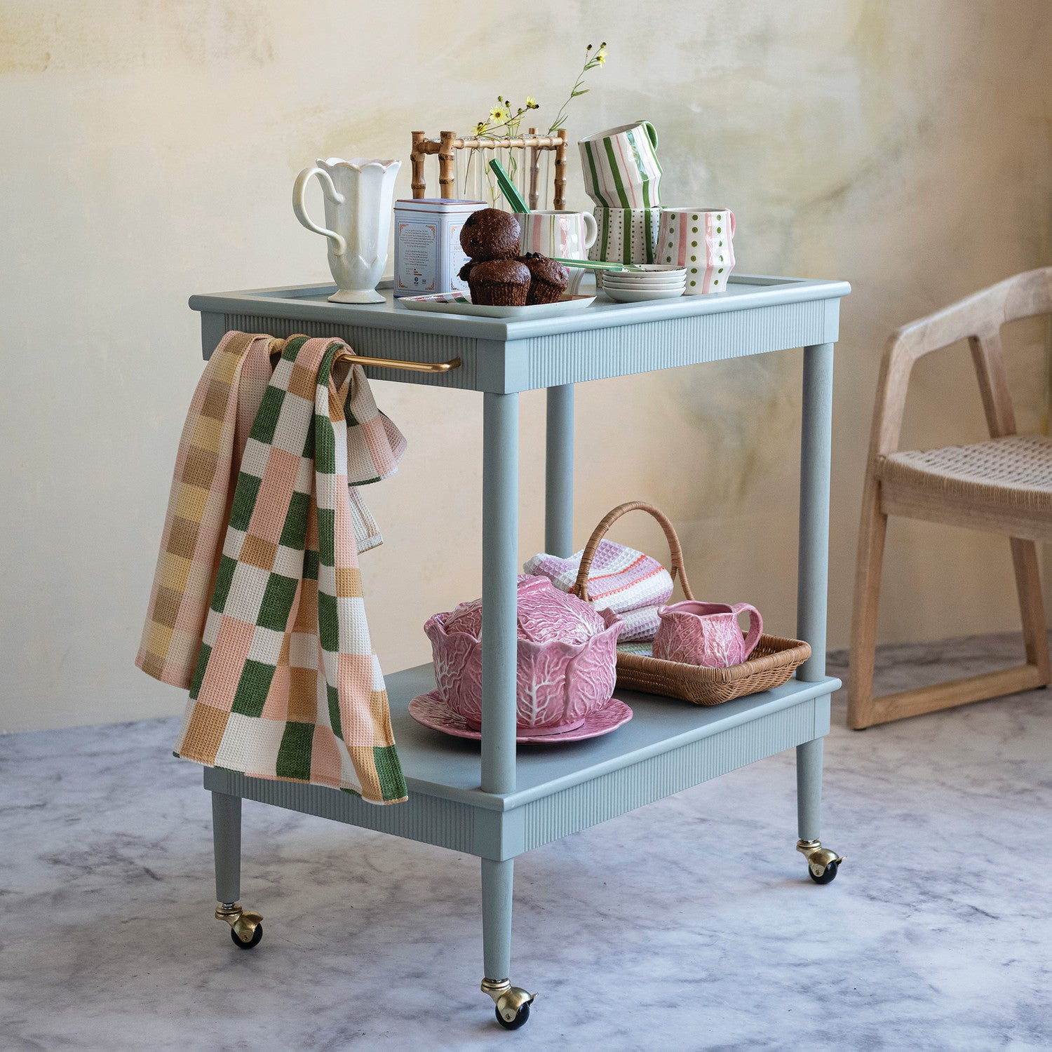 Light blue rolling cart with tea set and plaid towel in a room setting