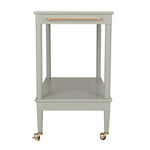 A light sage green two-tier side table with a single drawer on top featuring a copper-toned metal handle, supported by four legs with brass caster wheels.