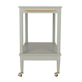 A light sage green two-tier side table with a single drawer on top featuring a copper-toned metal handle, supported by four legs with brass caster wheels.