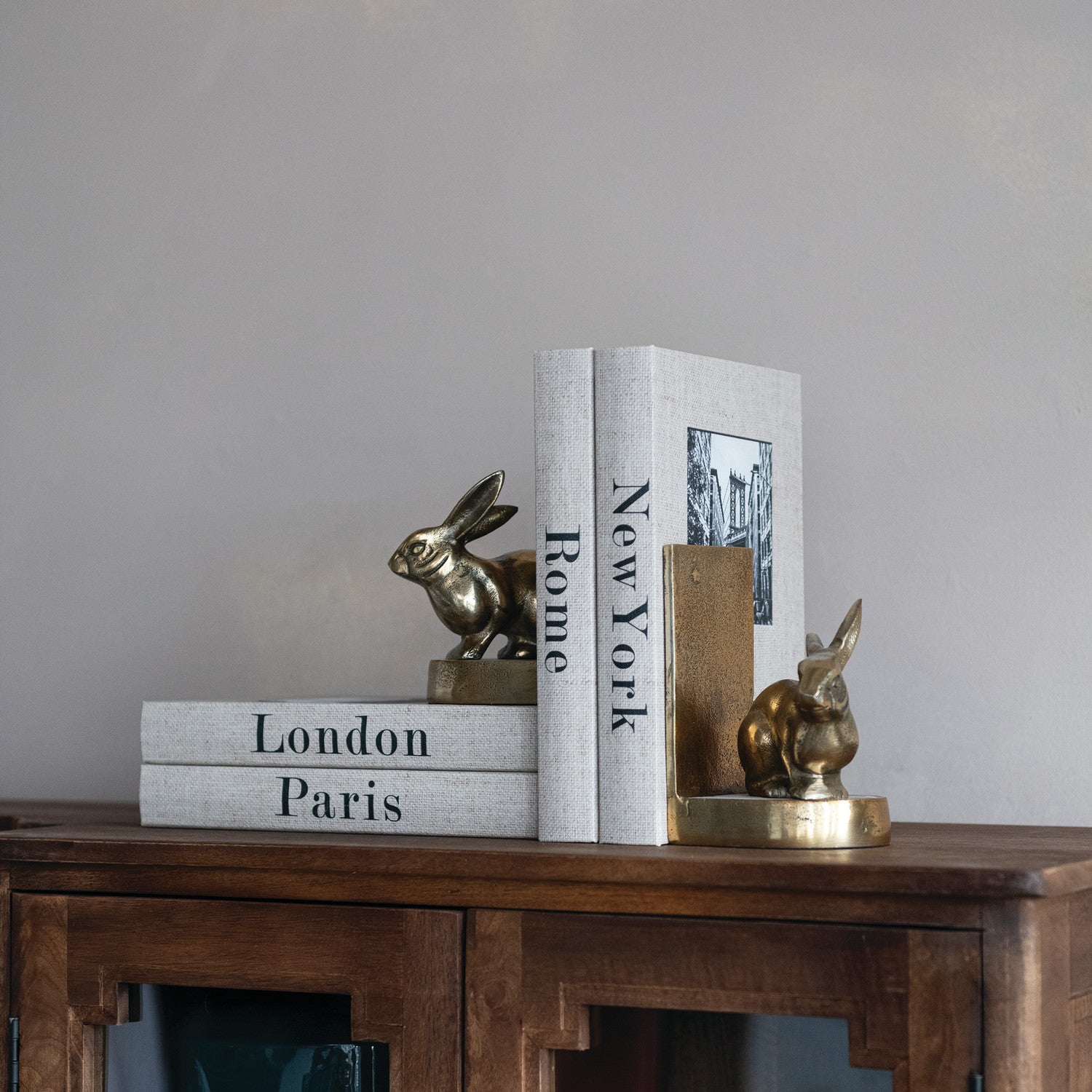 Decorative storage boxes shaped like books with rabbit sculptures on a wooden table against a gray wall.