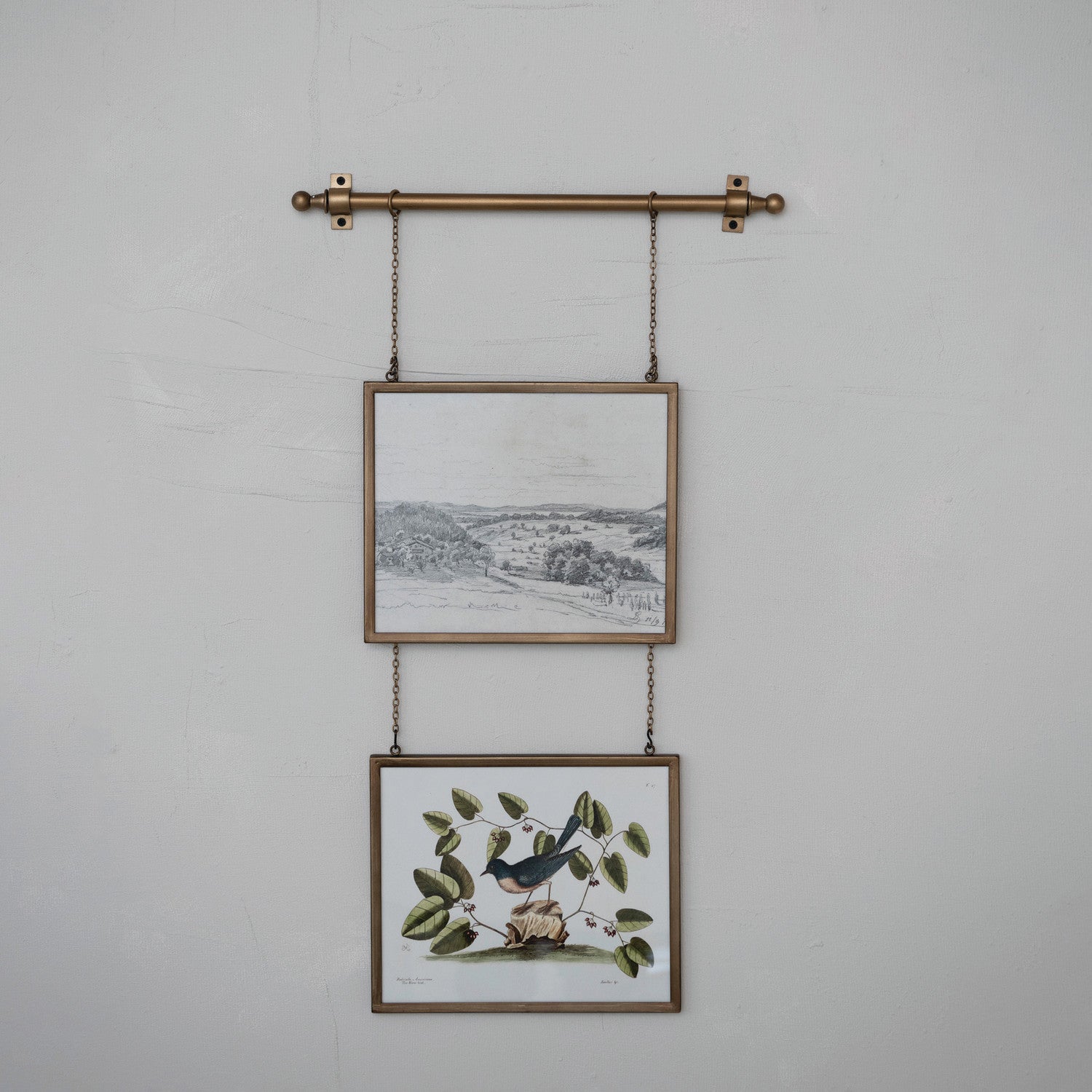 Two framed prints hanging on a wall with a decorative metal rod and chains.