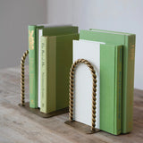 Green books held open by a decorative gold bookend on a wooden surface.