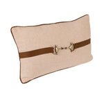 A rectangular beige textured lumbar pillow with a brown leather strap across the center featuring a horsebit hardware accent, shown on a plain white background.