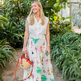 Woman in a white blouse and colorful skirt standing in a greenhouse holding a Montemare Palma Crossbody with orange leather accents