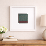 Framed artwork of a book on a wall above a wooden surface with decor items.
