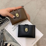 Brown and black wallets with gold buckles held by a hand on top of a magazine.