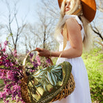 Woman holding a floral-patterned bag with a blurred background of trees and flowers
