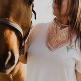 Woman wearing a pink bandana with horse designs, standing close to a horse.