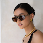 Woman wearing leopard print sunglasses and a gold necklace against a plain background