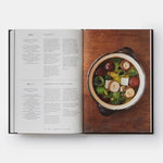 Open cookbook showing a page with text and a photograph of a bowl of soup on a wooden surface.