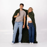 Two people standing under a large green camouflage-patterned blanket on a white background