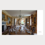 Dining room with long wooden table set for dinner, ornate chandelier, and classical decor.