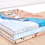 Stack of travel books with images of Italy on a beige surface