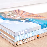 Stack of travel books with images of Italy on a beige surface