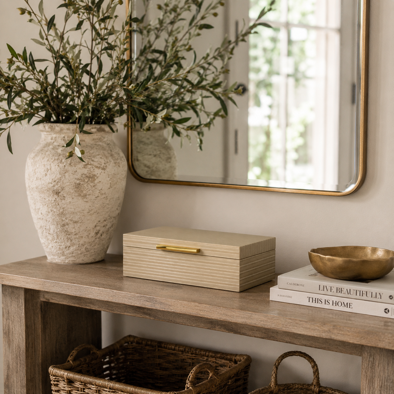 Decorative setup on a wooden console table with a vase, mirror, books, and baskets.