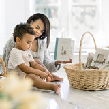 Woman and child sitting at a table with a book, surrounded by wicker baskets.