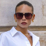 Woman wearing sunglasses and a white shirt against a beige wall.