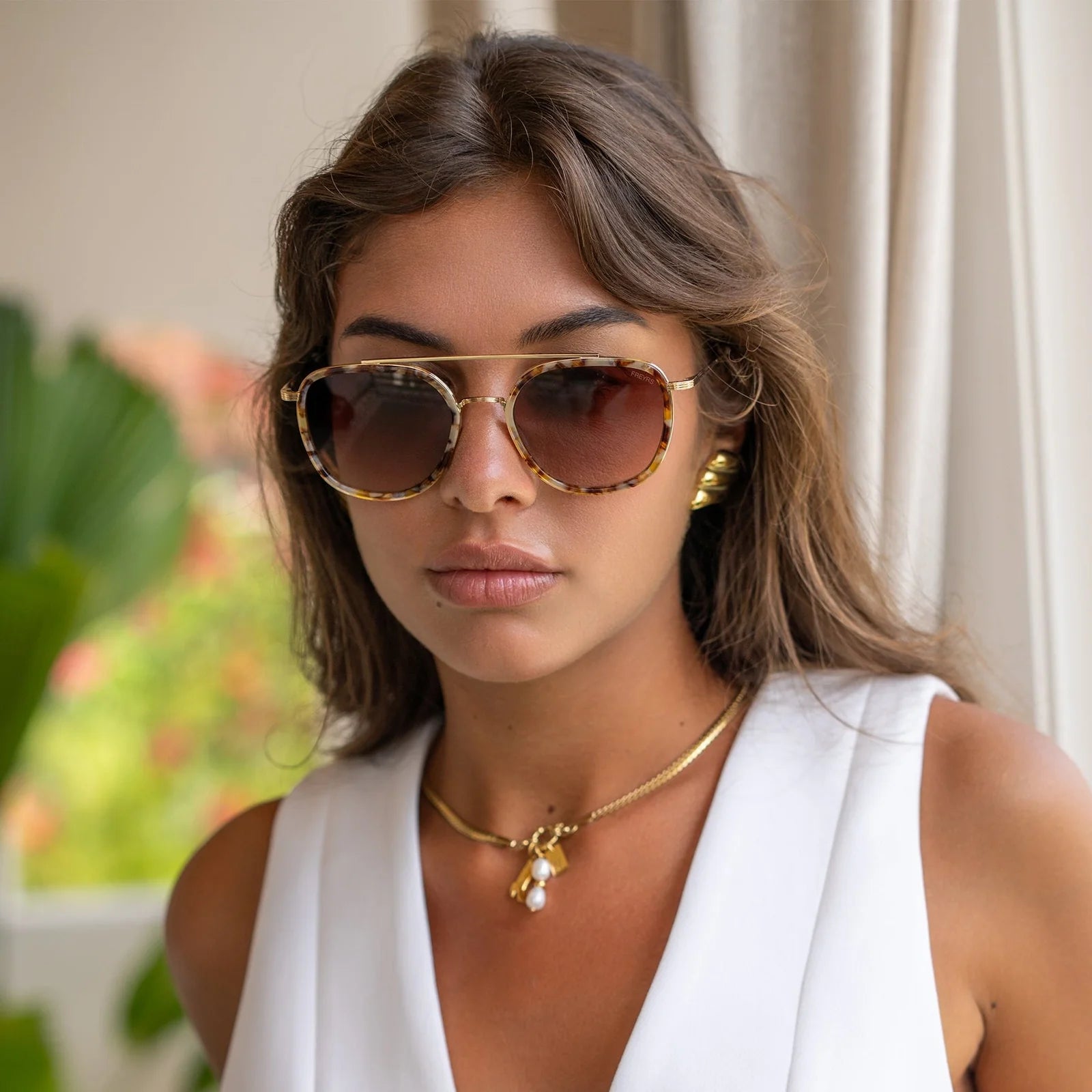 Woman wearing sunglasses and a white top with a blurred outdoor background