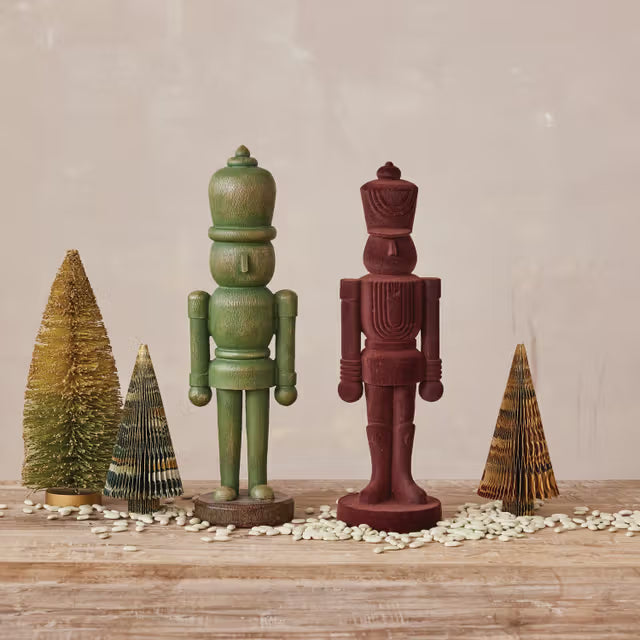 Two wooden nutcrackers and two small Christmas trees on a wooden surface with a neutral background.