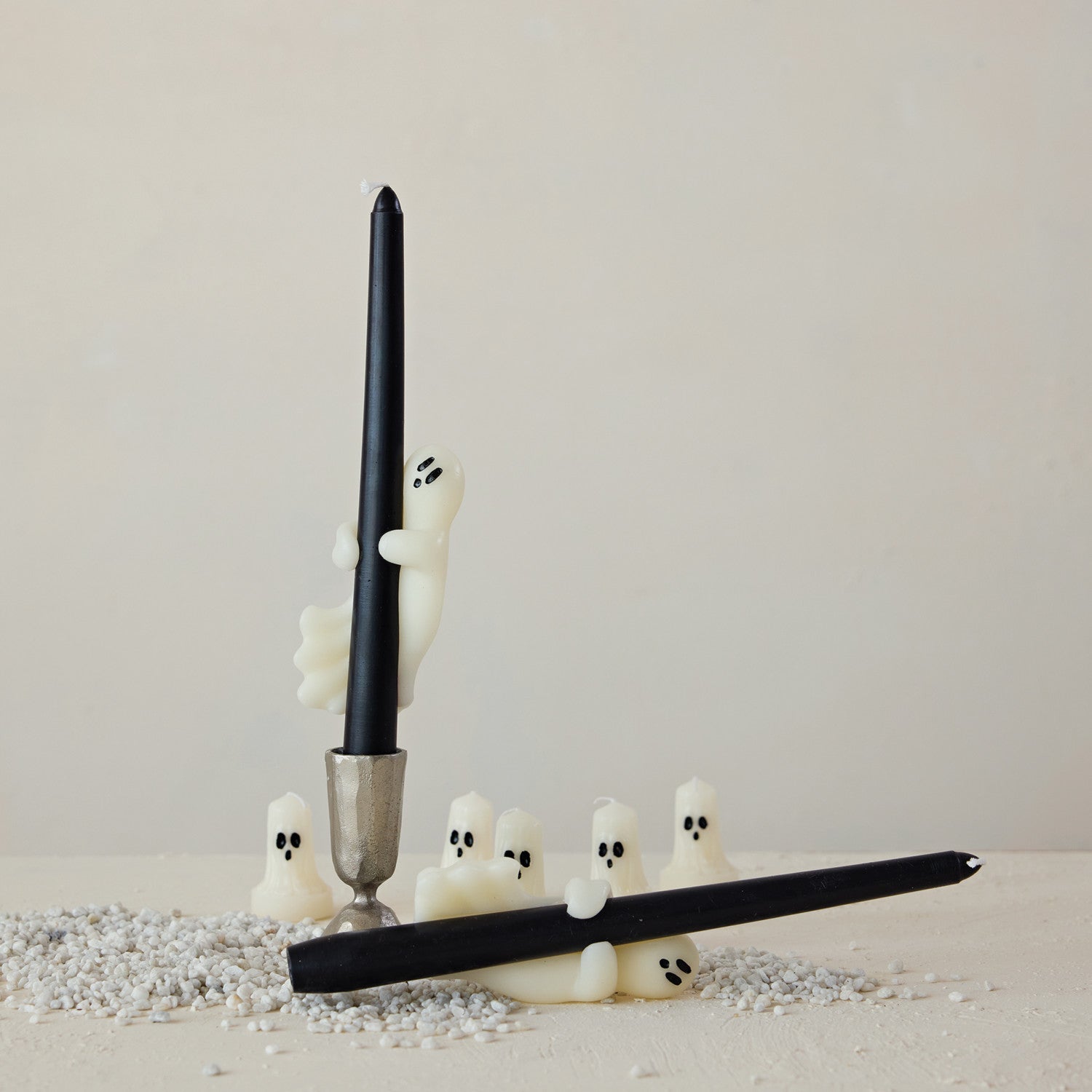 Black candle with ghost-shaped candle holders on a neutral background