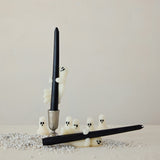 Black candle with ghost-shaped candle holders on a neutral background