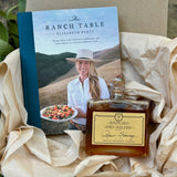 Book titled 'The Ranch Table' by Elizabeth Porte with a bottle of 'Rancho San Julian Raw Honey' on a textured surface.