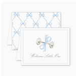 Folded greeting card with a watercolor-style silver baby rattle tied with a blue bow and the text “Welcome Little One” on the front; back features a blue bow lattice pattern. Card is blank inside and includes a Euro flap envelope.