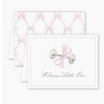 Folded greeting card with a watercolor-style silver baby rattle tied with a pink bow and the text “Welcome Little One” on the front. Card is blank inside and includes a Euro flap envelope.