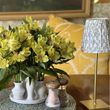Bouquet of yellow flowers in a white vase on a table with lamp and decorative items.