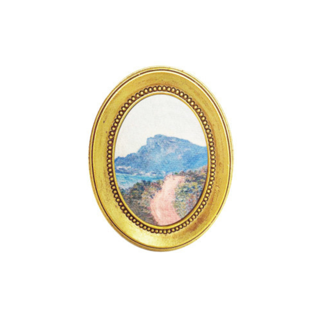 Gold-framed oval art magnet of a mountain landscape on a white background