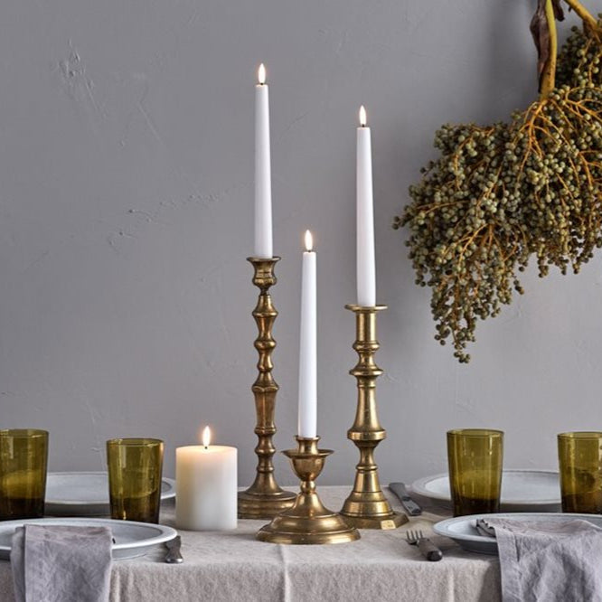 Table setting with candles, glasses, and a decorative plant against a gray wall.