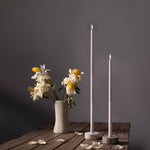 Two tall white candles and a vase with flowers on a wooden surface against a dark background