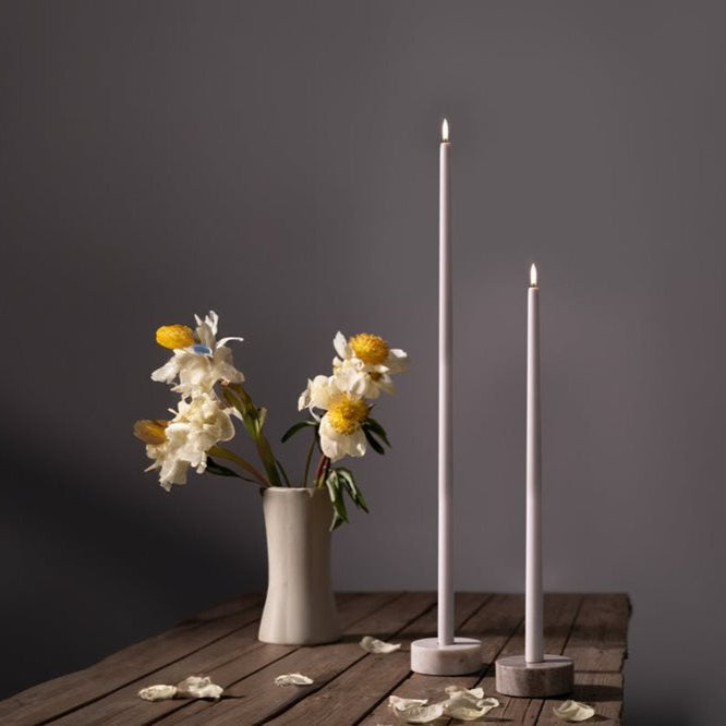 Two tall white candles and a vase with flowers on a wooden surface against a dark background