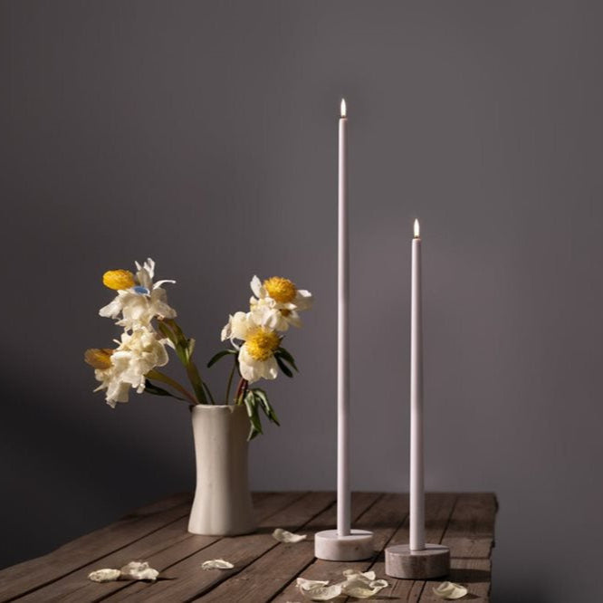 Two tall white candles and a vase with flowers on a wooden surface against a dark background