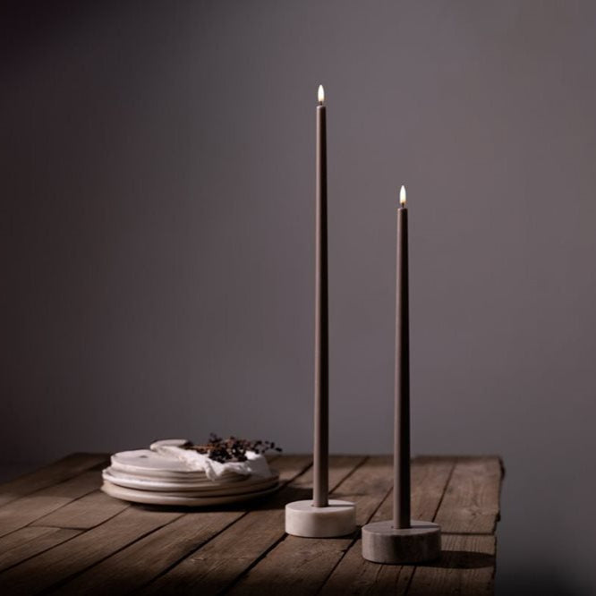 Two tall black candles on a wooden stand against a dark background