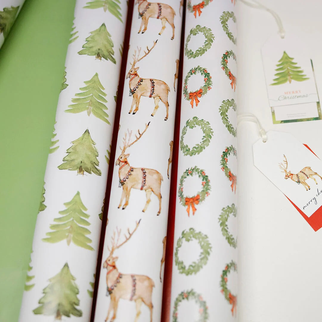 Rolls of Christmas-themed wrapping paper with reindeer, trees, and wreaths on a white background.