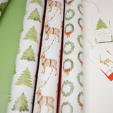 Rolls of Christmas-themed wrapping paper with reindeer, trees, and wreaths on a white background.