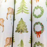 Three rolls of Christmas-themed wrapping paper with deer, trees, and wreaths.