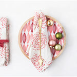 Wooden plate with a red and white patterned napkin, gold fork, and colorful ornaments on a white background.