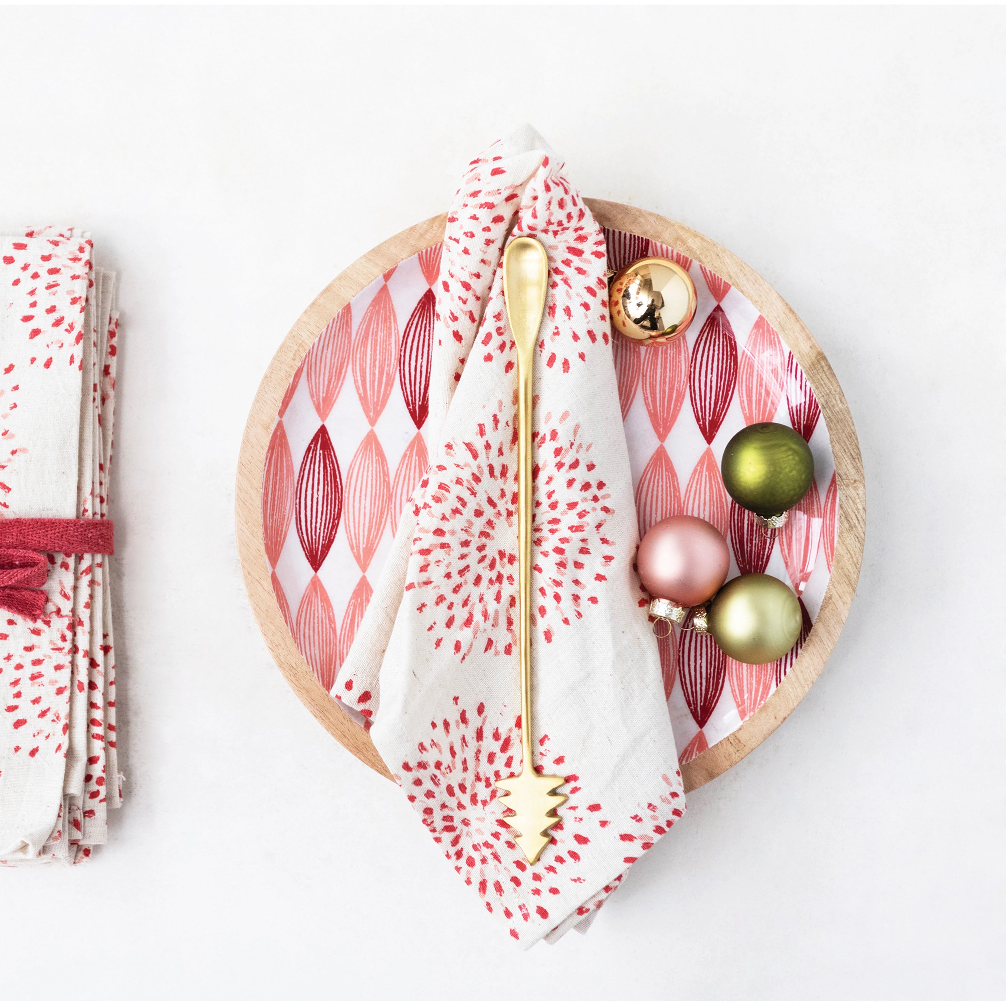 Wooden plate with a red and white patterned napkin, gold fork, and colorful ornaments on a white background.