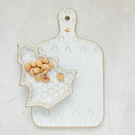 Decorative ceramic cutting board with a small bowl of nuts on a light background