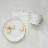 White ceramic mug and plate with decorative patterns on a light gray surface